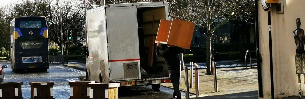 Mover carrying a wooden cabinet into the back of a white moving van on a city street