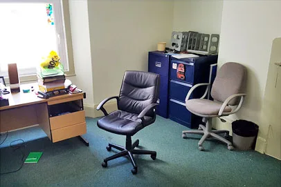 Small office with two chairs, a desk, and filing cabinets near a window.
