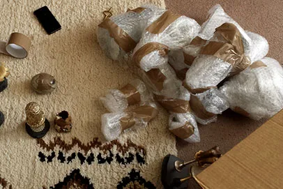 Decorative golden ornaments on a carpet with bubble-wrapped items and packing tape nearby.
