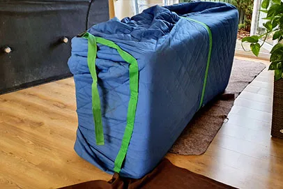 Furniture wrapped in a blue moving blanket secured with green straps, placed on a wooden floor.