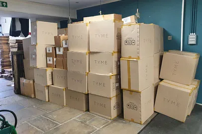Stacked cardboard boxes labeled "TYME" in a storage or warehouse area