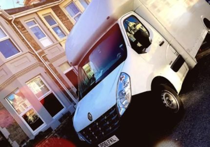 White moving van parked on a residential street with lens flare effects in the foreground.