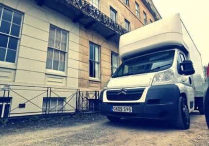 White moving van parked outside a historic stone building.